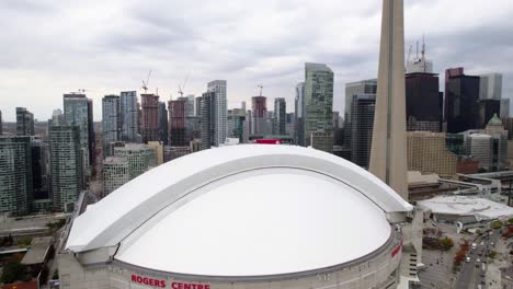 Aerial-view-of-the-Rogers-centre-and-the-CN-tower-in-cloudy-Toronto,-Canada---circling,-tilt,-drone-shot