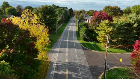 Cars-drive-on-road-through-American-suburbs-in-autumn