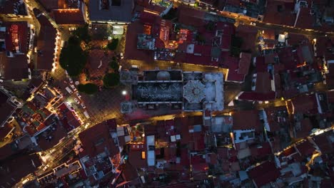 Illuminated-church-of-Santa-prisca-de-Taxco,-evening-in-Mexico---birds-eye,-aerial-view
