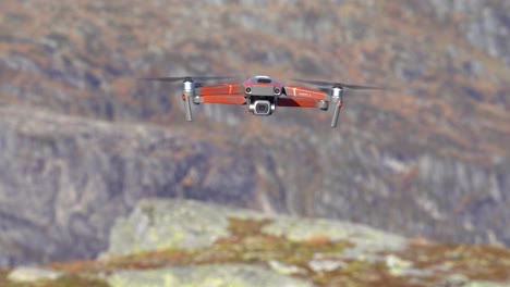 Drone-with-modern-camera-hovering-close-to-camera-before-moving-backwards-and-disappearing-into-blurred-mountain-landscape-background---Nesheim-mountain-in-Vaksdal-Norway