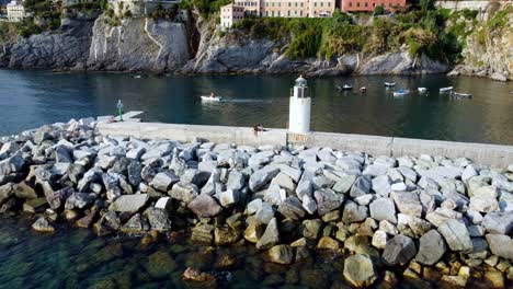 Dronie-Shot-Of-Couple-Sitting-Next-To-Lighthouse-in-Camogli-,-Famous-Attraction,-Genova