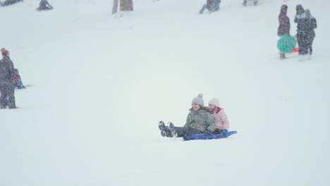 Two-kids-sledding-down-a-snow-covered-hill-during-winter