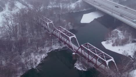 Luftaufnahme-Einer-Bahngleisbrücke,-Die-Einen-Fluss-Mit-Schnee-überquert,-Der-Den-Boden-Bedeckt