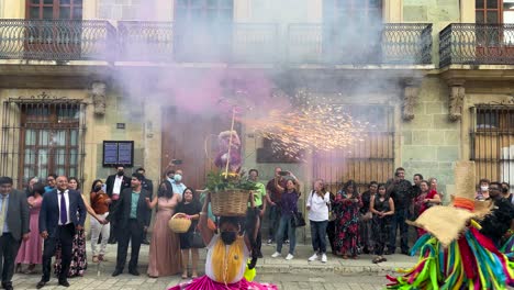 Toma-En-Cámara-Lenta-De-Una-Mujer-Indígena-Con-Los-Trajes-Tradicionales-De-Hombre-Pájaro-Oaxaca-Y-Fuegos-Artificiales-Morados-En-La-Cabeza-Durante-Una-Celebración-De-Boda-En-La-Ciudad-De-Oaxaca-México