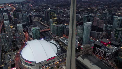 Aerial-view-in-front-of-the-CN-tower-and-the-Rogers-centre-in-downtown-Toronto,-gloomy-evening-in-Ontario,-Canada---tilt,-drone-shot