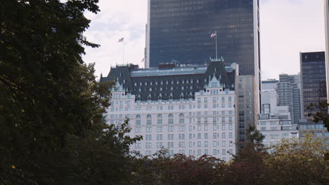 Blick-Auf-Das-Plaza-Hotelgebäude-über-Den-Central-Park,-New-York-City,-Manhattan,-USA,-Die-Vegetation-Der-Städtischen-Parkbäume-Im-Vordergrund-Und-Die-Modernen-Gebäudetürme-Der-Innenstadt-Im-Hintergrund
