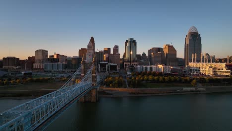 Aerial-view-over-the-Ohio-river,-towards-the-Cincinnati-cityscape,-vibrant,-autumn-sunset---rising,-drone-shot