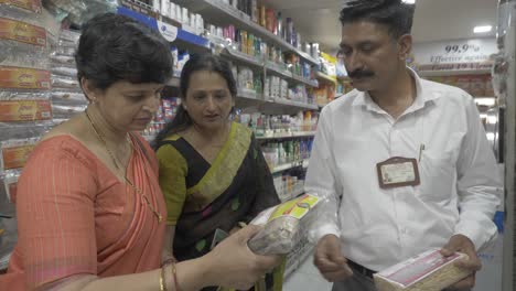 Ein-Supervisor-Für-Verbraucherangelegenheiten-Klärt-Zwei-Indische-Frauen-Mittleren-Alters-über-Den-Einkauf-Von-Einzelhandelsartikeln-Mit-Irreführenden-Verpackungspraktiken-Auf