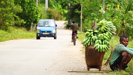 Vietnamesischer-Mann,-Der-Sich-Am-Straßenrand-Mit-Einem-Korb-Voller-Grüner-Bananen-Ausruht
