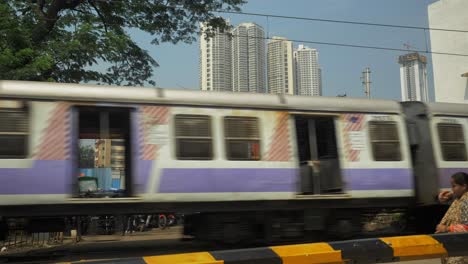 Toma-Estática-Del-Cruce-Del-Tren-Local-En-Velocidad-A-Través-Del-Cruce-Ferroviario-En-Wadala-Más-Tarde-La-Gente-Cruza-La-Vía,-Mumbai