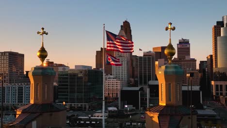 Aerial-view-around-the-US-and-Ohio-flag-waving-with-city-background,-sunset-in-USA---slow-motion