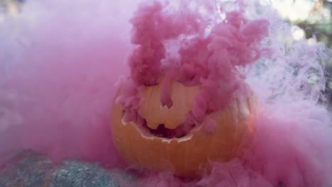 Geschnitzter-Halloween-Kürbis-Mit-Rosafarbenem-Rauch,-Der-Aus-Dem-Gesicht-Der-Jack-o-Laterne-Kommt,-Für-Einen-Gruseligen-Effekt-In-Zeitlupe,-Draußen-Im-Wald