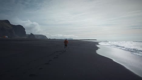 Tracking-Shot-Of-Athletic-Man-Running-On-Black-Beach,-Reynisfjara,-Iceland