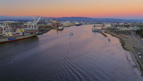 Aerial-view-following-San-Francisco-Alameda-ferry-navigating-Oakland-maritime-port-at-sunset