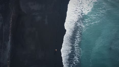 Stunning-Over-headshot-Of-Man-Running-On-Sandy-Black-Beach-Near-Waves,-Iceland