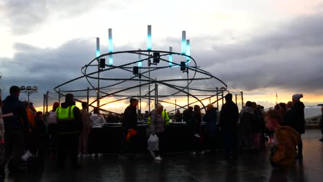 Crowd-interact-with-illuminated-spiral-light-looper-neuron-artwork,-Liverpool-pier-head-river-of-light-event-at-sunset