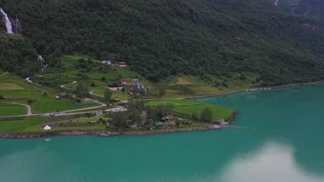 Yrineset-camping-along-Oldevatn-glacial-lake-in-Olden-Norway---Aerial-above-lake-looking-towards-fantastic-campsite-with-waterfalls-and-lush-mountainside-in-background