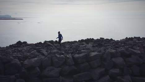 Girl-Hiking-Carefully-On-Black-Volcanic-Rocks-In-Ocean-Background,-Black-Beach,-Iceland
