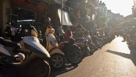 POV-Riding-Past-Rows-Of-Parked-Motorbikes-And-Scooters-For-Hire-In-Hanoi-With-Golden-Yellow-Sun-Flares-Light