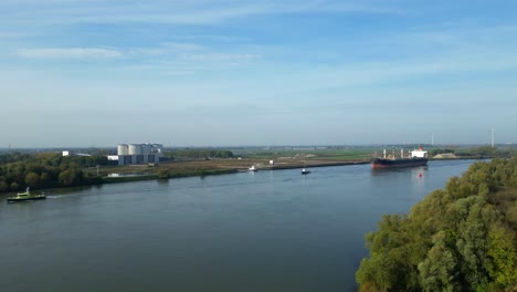 Aerial-Flying-Over-Tree-Line-Towards-Oude-Maas-With-View-Of-Tug-Boats-Assisting-Sea-Prajna-Bulk-Ship-Along-In-Puttershoek