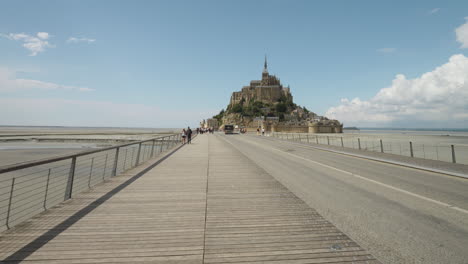 Walking-On-The-Footbridge-Of-Mont-Saint-Michel-During-Sunny-Day-In-Normandy,-France