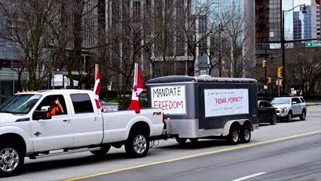handheld-shot-of-pan-shot-of-a-white-truck-with-Canadian-flags-and-a-trailer-during-trucker-convoy-protest-in-downtown-Vancouver