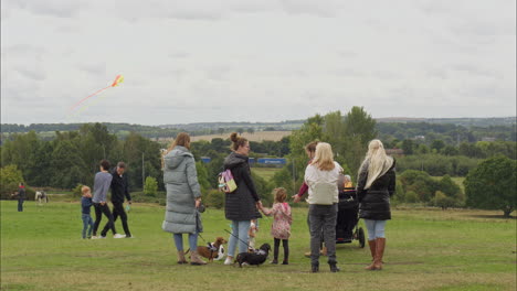Mothers-with-children-stood-watching-kites-flying-at-a-Kite-festival-on-Heath-Common-Wakefield,-dull-spring-day