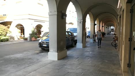 Señora-Caminando-Sobre-Pavimento-Debajo-De-Arcos-En-Una-Ciudad-En-Italia