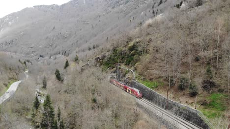 Aerial:-passenger-red-train-emerging-from-a-tunnel-in-the-Pyrenees,-southern-France