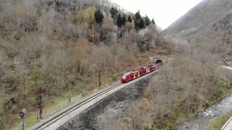 Aerial:-passenger-red-train-entering-a-tunnel-in-the-Pyrenees,-southern-France