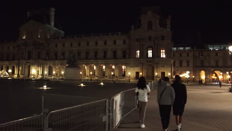 People-Walking-Along-The-Courtyard-During-Night-At-Louvre-Museum-A-Historic-Landmark-In-Paris,-France