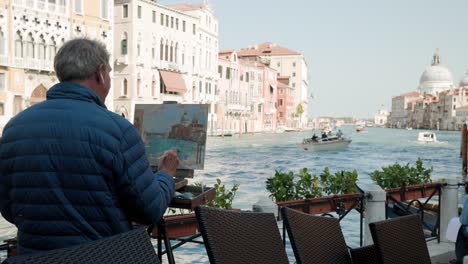 Old-Man-Artist-On-A-Balcony-Painting-Views-Along-The-Famous-Grand-Canal-In-Venice,-Italy