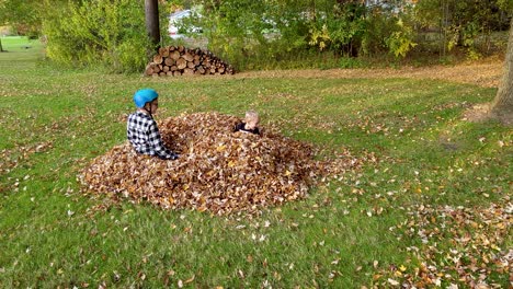 Two-Kids-Jumping-Joyfully-Into-Pile-Of-Fallen-Leaves-In-Autumn-Season