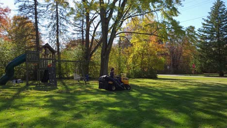 Young-Girl-Driving-Yellow-Tractor-In-Beautiful-Green-Yard-With-Small-Playground