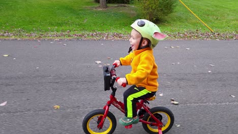Lindo-Niño-Feliz-En-Bicicleta-Rápido-Con-Entusiasmo-En-La-Calle-En-La-Temporada-De-Otoño