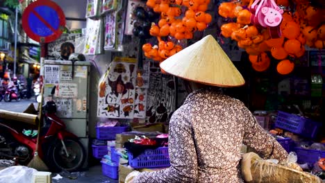 Traditional-Vietnamese-Woman-Wearing-Conical-Hat-Carrying-Goods-Walking-Past-Halloween-Store-In-Hanoi