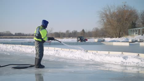 Maintenance-worker-spraying-water-on-an-outdoor-ice-rink,-slow-motion