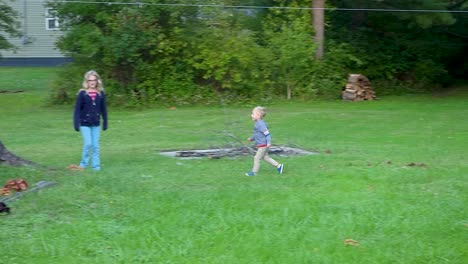 Little-Kid-With-His-Older-Sister-Playing-Out-On-Green-Grass-Next-To-Huge-Tree-Trunk