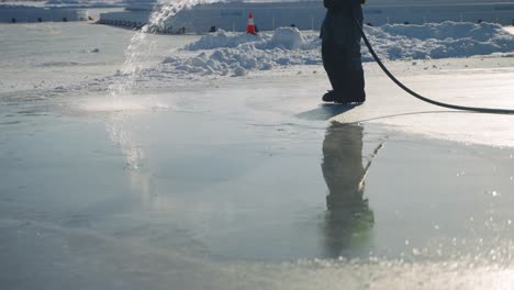 Worker-spraying-water-to-smooth-outdoor-ice-rink-surface,-slow-motion