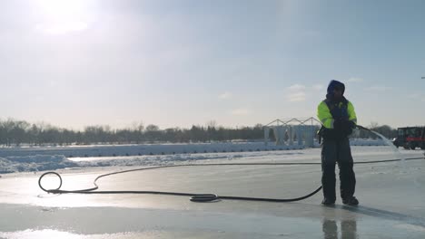 Maintenance-worker-spraying-water-onto-outdoor-lake-ice-rink