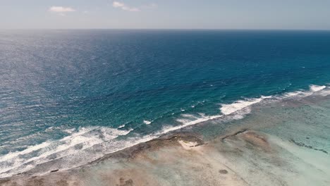 Aerial-view-pan-right-waves-crash-on-barrier-reef,-los-roques-sebastopol