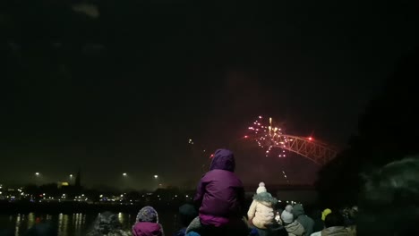Crowd-watch-colourful-fireworks-flash-on-Silver-Jubilee-bridge,-Widnes