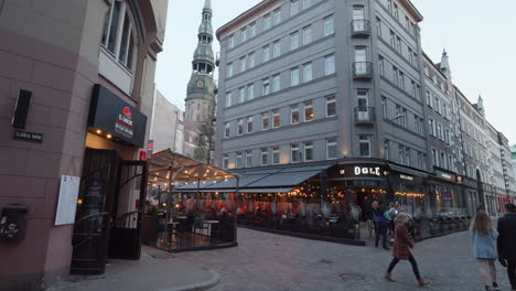 People-Walking-In-The-Street-Passing-By-Trendy-Restaurant-At-The-Street-Corner-In-Riga,-Latvia-At-Dusk