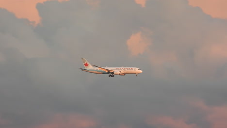 Air-Canada-airplane-flying-through-sunset-sky-with-pink-cloud-in-the-back