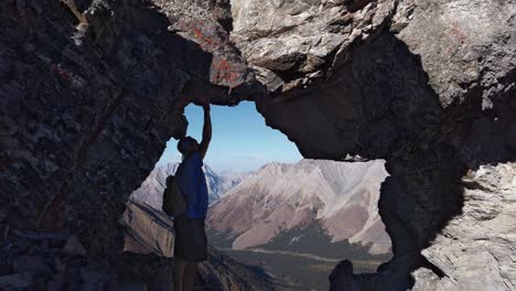 Wanderer,-Der-Den-Felsen-Berührt-Und-Den-Blick-Durch-Den-Lochbogen-Auf-Dem-Berg-Kananaskis,-Alberta,-Kanada,-Bewundert