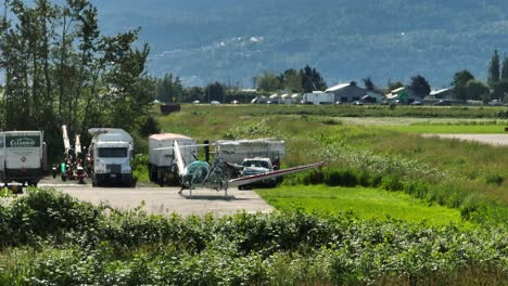 Airport-Vehicles-With-Helicopter-Spinning-Its-Main-Rotor-Near-The-Chilliwack-Airport-In-BC,-Canada