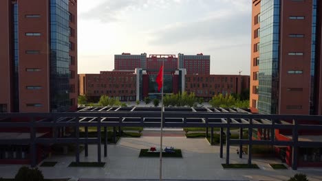Flying-Chinese-flag,-aerial-ascending-forward-dolly-view-taken-at-Beijing-Jiaotong-University-in-2020