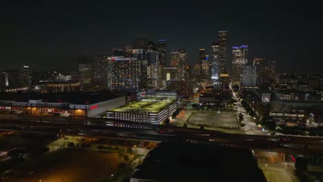 Aerial-view-over-traffic-on-interstate-69,-towards-Houston-city-skyscrapers,-night-in-Texas,-USA---rising,-drone-shot