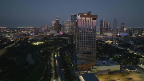 Aerial-view-passing-the-Allen-high-rise-and-Eleanor-Tinsley-Park-with-downtown-Houston-in-the-background,-dusk-in-Texas,-USA