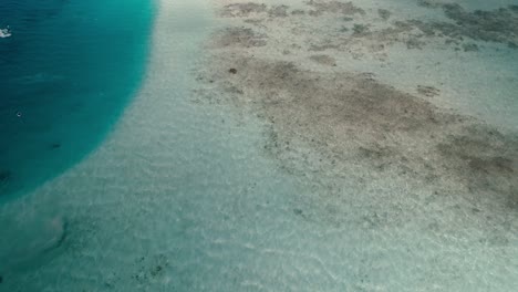 Aerial-view-tilt-up-reveal-barrier-reef-kiters-sailing-on-blue-shalow-water,-Los-Roques